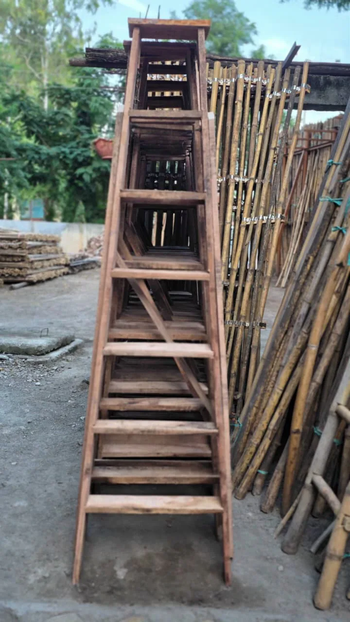 Wooden frame ladder standing upright in a yard beside stacked bamboo poles